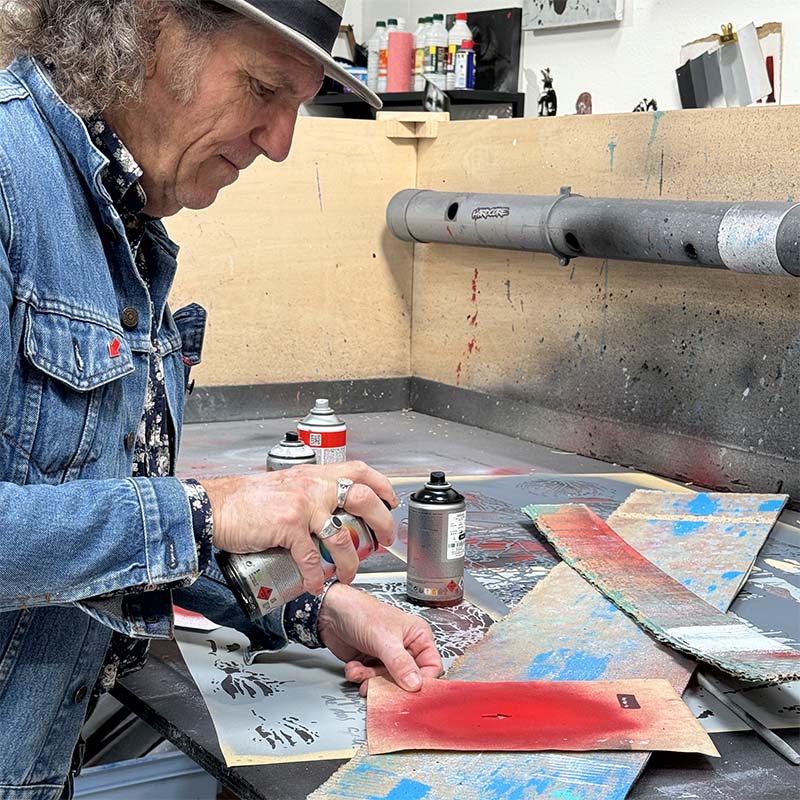 Jef Aérosol dans son atelier, en train de pulvériser de la peinture sur un pochoir